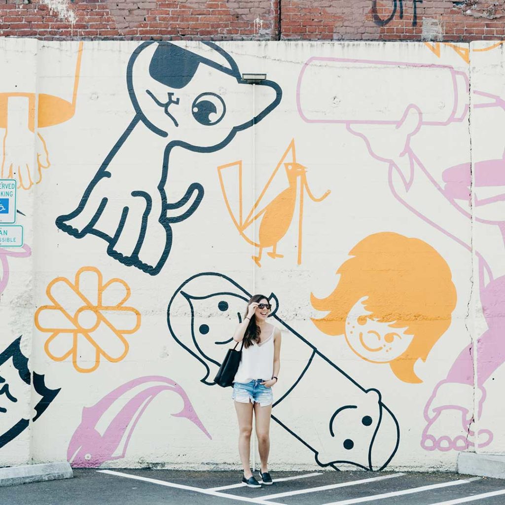 woman with sunglasses in front of mural in parking lot in portland oregon