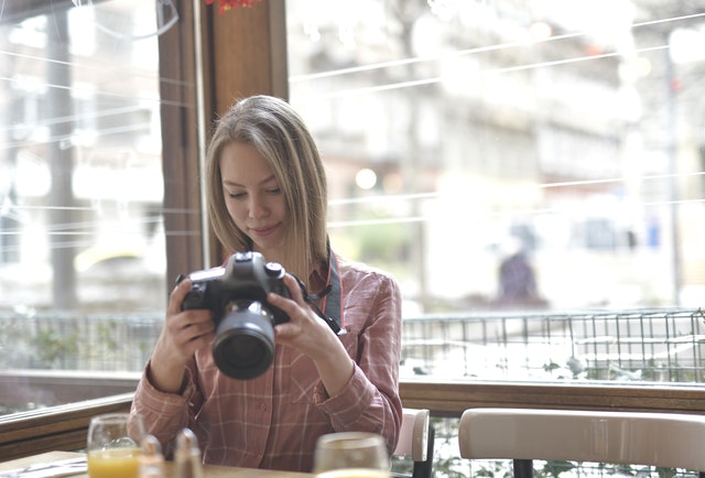 Young female photographer with photo camera sitting in cafe